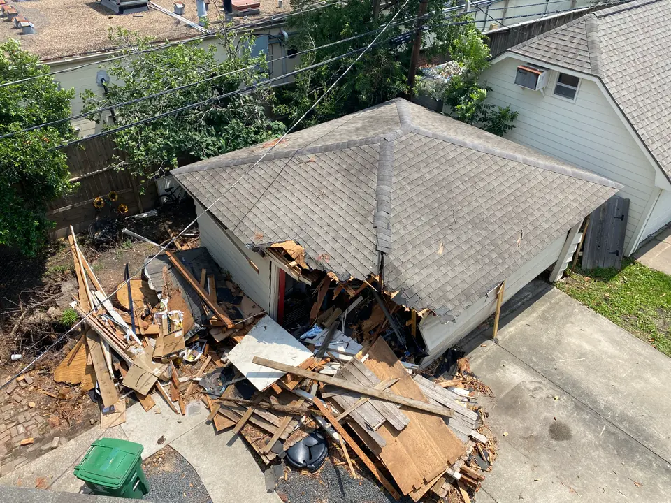 Collapsed garage wall and debris beside a shingle-roofed building